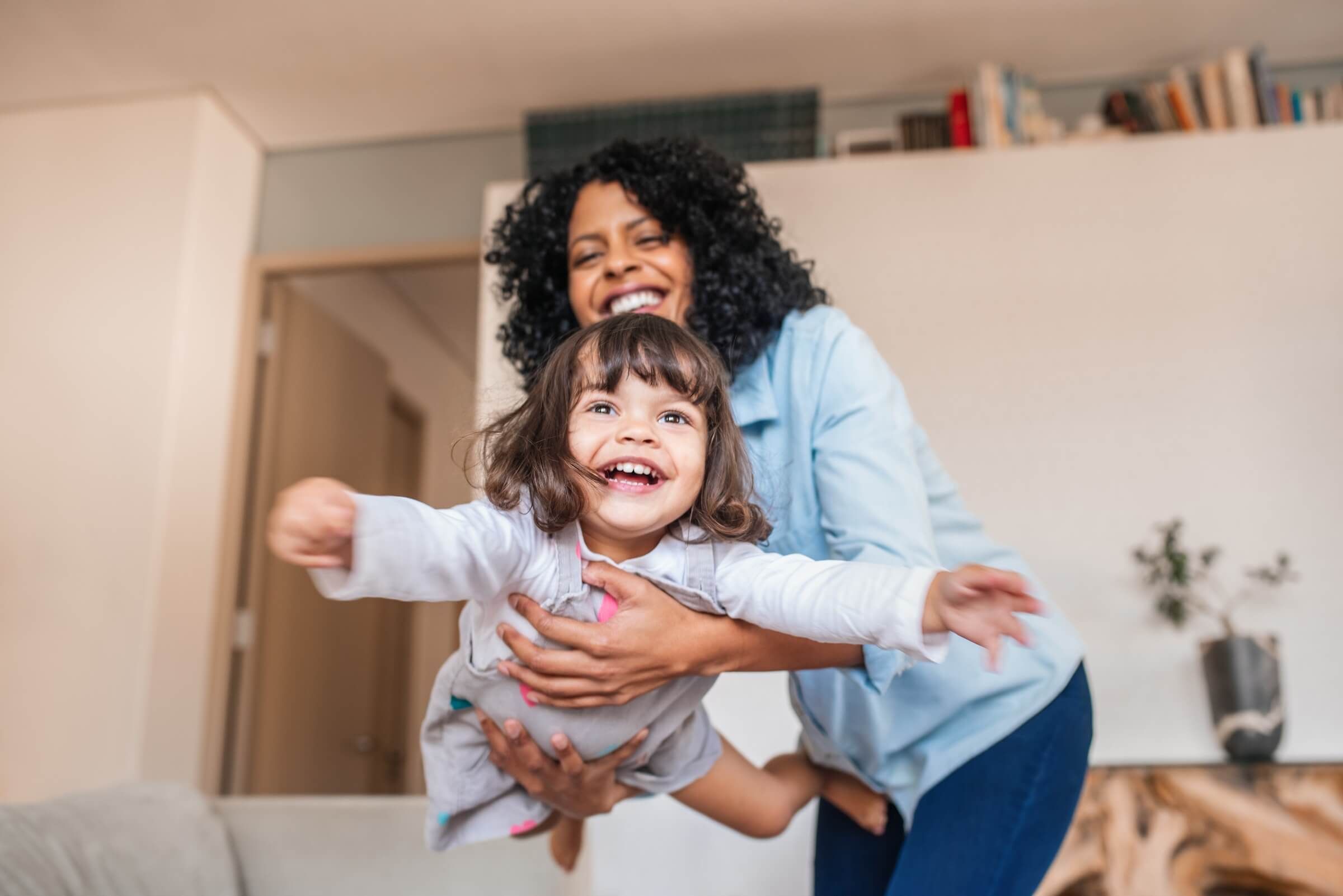 A parent lifting a laughing child through the air at home