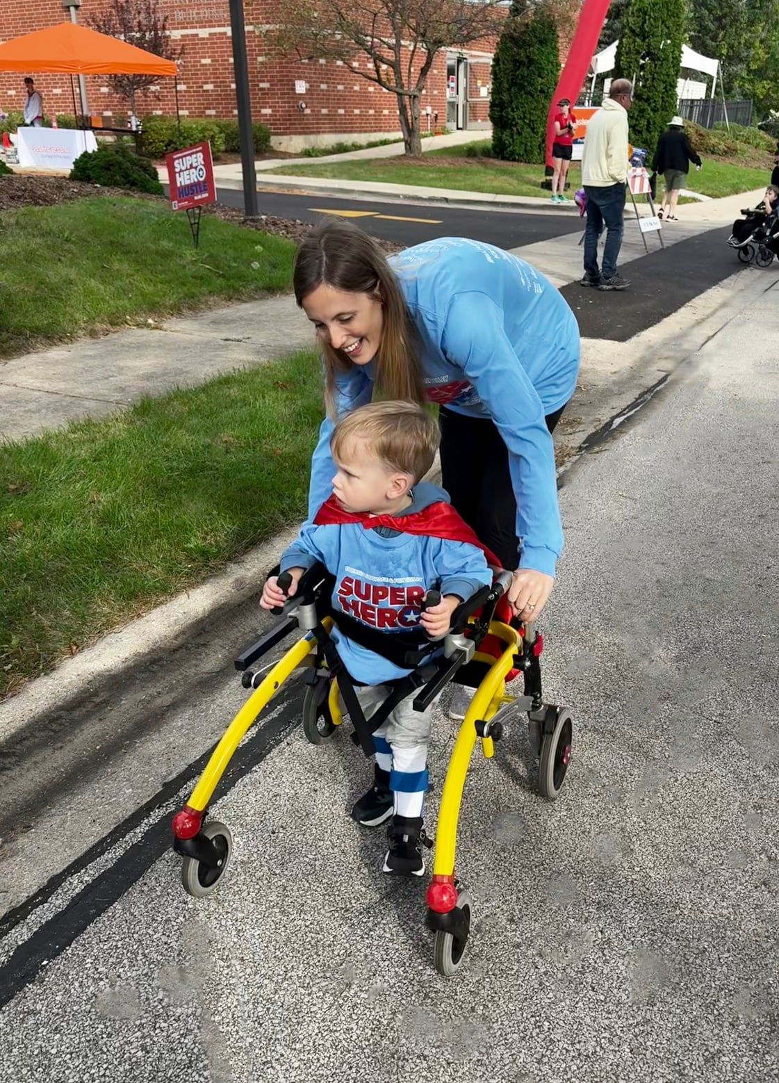 Tierney walking beside her son as he uses his walker, wearing a superhero cape